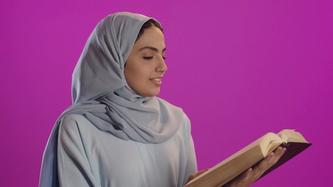 قراءة الكتب بتمعن, إيماءات التركيز والاندماج ، ثقافة التعلم الذاتي, بورتريه لامرأة عربية خليجية سعودية ترتدي العباءة الرمادية والحجاب تحمل بيدها كتاب تثقيفي , الاستمتاع بقراءة الروايات والقصص, خلفية بنفسجية