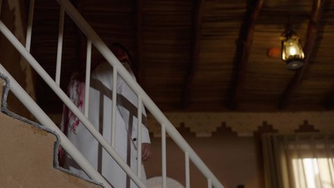 استخداد السلم داخل المنزل العصري، الاهتمام بالمظهر الخارجي، النظر إلى الكاميرا بايماءات بفخر واعتزاز ، مفهوم الرجولة والأناقة، رجل داخل منزل عصري ، تصوير  لسيد عربي خليجي سعودي يرتدي الثوب الابيض والشماغ يسير بين المنازل، نظارة طبية على عينيه