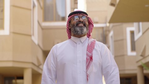 التأمل والتعمق في تفاصيل المبنى الخارجي للمنزل، رجل عند مدخل منزل عصري ،  سيد عربي خليجي سعودي يرتدي الثوب الابيض والشماغ يسير بين المنازل، نظارة طبية على عينيه، الاهتمام بالمظهر الخارجي، مفهوم الرجولة والأناقة، الوقوف بفخر واعتزاز بالدولة السعودية