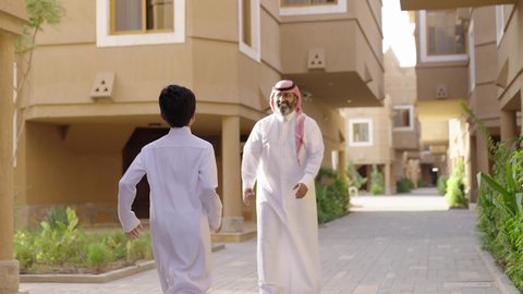 قضاء وقت ممتع مع الأطفال, مشاركة اللحظات السعيدة والتسلية مع الأبناء, الاستمتاع باللعب مع العائلة، عائلة عند مدخل منزل عصري ، مفهوم الأسرة السعيدة، طفل يرتدي الثوب الأبيض،  أب عربي خليجي سعودي يرتدي الثوب الابيض والشماخ يمسك يحمل ابنه ويلعب معه