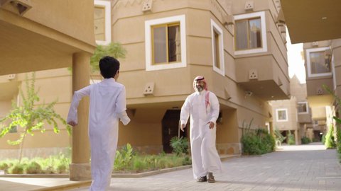 مشاركة اللحظات السعيدة والتسلية مع الأبناء, الاستمتاع باللعب مع العائلة، عائلة عند مدخل منزل عصري ، مفهوم الأسرة السعيدة، طفل يرتدي الثوب الأبيض، قضاء وقت ممتع مع الأطفال, أب عربي خليجي سعودي يرتدي الثوب الابيض والشماخ يمسك يحمل ابنه ويلعب معه