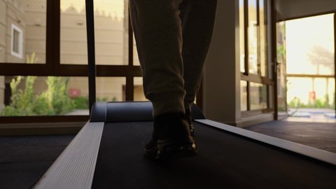 القيام بالأنشطة الترفيهية الممتعة، المحافظة على الصحة واللياقة البدنية, استخدام الاجهزة الرياضية، ممارسة تمارين الاحماء,  شاب عربي خليجي سعودي يرتدي الملابس الرياضية يقوم بالمشي على الجهاز الكهربائي، نادي الألعاب الرياضية