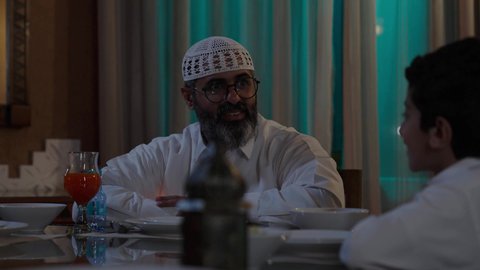 تقديم الطبق الرئيسي ووضعه على السفرة، أداء فريضة الصيام في شهر رمضان المبارك، قضاء أوقات ممتعه مع الأهل والأبناء، تبادل الأحاديث بين أفراد الأسرة، طفل عربي خليجي سعودي مجتمع مع عائلته حول مائدة الطعام، سفرة مليئة بأصناف من المأكولات الشرقية الشهية