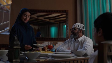 ملئ الأطباق بماهو مطلوب من الطعام , أداء فريضة الصيام في شهر رمضان المبارك، قضاء أوقات ممتعه مع الأهل والأبناء، تبادل الأحاديث بين أفراد الأسرة، طفل عربي خليجي سعودي مجتمع مع عائلته حول مائدة الطعام، سفرة مليئة بأصناف من المأكولات الشرقية الشهية