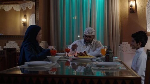 القاء الدعابة والهزاز خلال جلسة الطعام, أداء فريضة الصيام في شهر رمضان المبارك، قضاء أوقات ممتعه مع الأهل والأبناء، تبادل الأحاديث بين أفراد الأسرة، طفل عربي خليجي سعودي مجتمع مع عائلته حول مائدة الطعام، سفرة مليئة بأصناف من المأكولات الشرقية الشهية