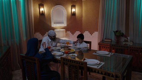 تبادل الأحاديث بين أفراد الأسرة، أجواء عائلية دينية رمضانية سعيدة، عائلة عربية خليجية سعودية مجتمعة حول مائدة الطعام، سفرة مليئة بأصناف من المأكولات الشرقية الشهية، أداء فريضة الصيام في شهر رمضان المبارك، زينة المناسبات الإسلامية