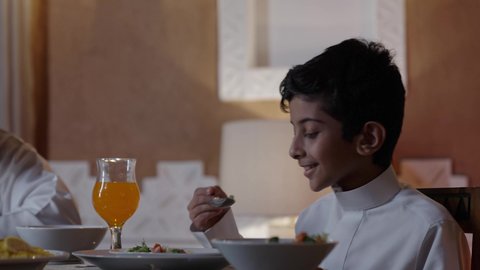 Spending enjoyable times with family and children, exchanging conversations among family members, happy religious family atmospheres during Ramadan, an Arab Gulf Saudi child gathered with his family around the dining table, a spread full of delicious Eastern dishes, performing the obligation of fasting in the blessed month of Ramadan.