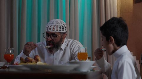 أجواء عائلية روحانية دينية إسلامية، ايماءات السرور لاجتماع العائلة حول مائدة إفطار رمضان، عائلة عربية خليجية سعودية مجتمعة حول مائدة الطعام، سفرة مليئة بأصناف من المأكولات الشرقية الشهية، أداء فريضة الصيام في شهر رمضان المبارك، موعد كسر الصيام عند الأذان