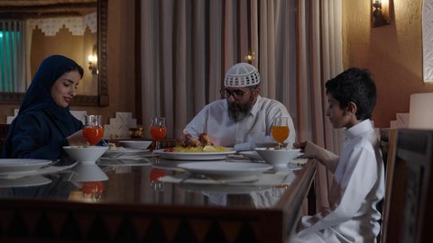 ايماءات السرور لاجتماع العائلة حول مائدة إفطار رمضان، أجواء عائلية روحانية دينية إسلامية، عائلة عربية خليجية سعودية مجتمعة حول مائدة الطعام، سفرة مليئة بأصناف من المأكولات الشرقية الشهية، أداء فريضة الصيام في شهر رمضان المبارك، موعد كسر الصيام عند الأذان