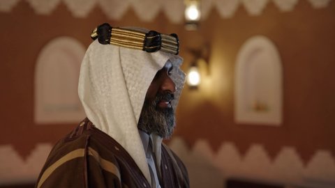 النظر للكاميرا بايماءات السرور، أزياء سعودية تقليدية شعبية، تصوير لرجل مسن عربي سعودي خليجي يرتدي الزي السعودي الشعبي التقليدي, الزي التراثي للمناسبات الوطنيه, التجول داخل منزل تراثي بتصميم عصري, بيوت تراثيه قديمه, شعبيات, أحياء أثريه قديمه, جوله بين الأحياء الشعبيه