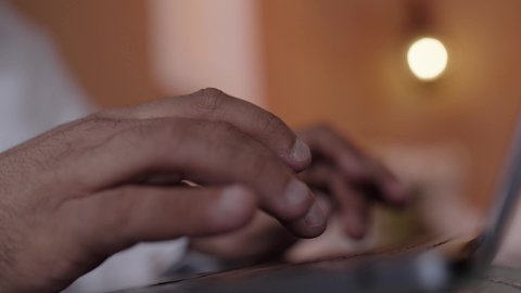 جهاز تقني حديث ومتطور، استخدام التقنية الحديثه المتطورة في الحياة العملية، ايماءات الاندماج والتركيز، تصوير مقرب لايدي رجل عربي خليجي سعودي يرتدي الثوب التقليديوالشماغ ويضع النظارة الطبية يجلس على الكرسي ويعمل على الحاسب المحمول في صالة المنزل، النظر الى شي ما