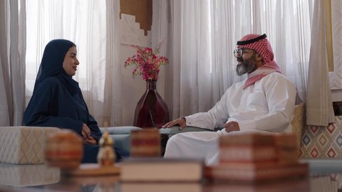 مفهوم الحب والحنان، دور الأب في حياه الأبناء، تصوير لأب كبي بالسن عربي خليجي سعودي يرتدي الثوب التقليدي والشماغ يجلس على كرسي وبجانبه ابنته تجلس، قضاء وقت ممتع ومسلي، ايماءات السعادة والسرور، اجواء اسرية مليئة بالفرح،التسامر وفتح الاحاديث