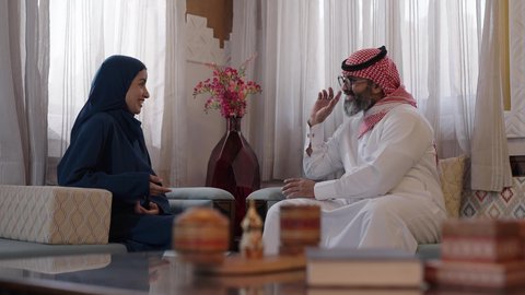 تبادل الاخبار والمعلومات، مفهوم الحب والحنان، دور الأب في حياه الأبناء، تصوير لأب كبي بالسن عربي خليجي سعودي يرتدي الثوب التقليدي والشماغ يجلس على كرسي وبجانبه ابنته تجلس، قضاء وقت ممتع ومسلي، ايماءات السعادة والسرور، التسامر وفتح الاحاديث