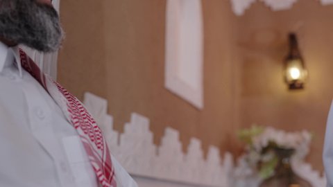 تعابير المودة والمحبة، دور الأب في حياه الأبناء،  الاستمتاع بقضاء وقت مع الابناء، رجل كبير بالسن عربي خليجي سعودي يرتدي الثوب التقليدي والشماغ يجلس على الاريكة بجانب ابنه  في غرفة الجلوس، التسامر وتبادل الاحاديث، جلسة عائلية سعيدة
