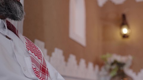 The father's role in his children's lives, enjoying time with his sons, an elderly Arab man from the Gulf region of Saudi Arabia wearing a traditional thobe and shemagh, sitting on the sofa next to his son in the living room, chatting and exchanging stories, a happy family gathering, expressions of affection and love.