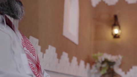 الاستمتاع بقضاء وقت مع الابناء، دور الأب في حياه الأبناء، رجل كبير بالسن عربي خليجي سعودي يرتدي الثوب التقليدي والشماغ يجلس على الاريكة بجانب ابنه  في غرفة الجلوس، التسامر وتبادل الاحاديث، جلسة عائلية سعيدة، تعابير المودة والمحبة