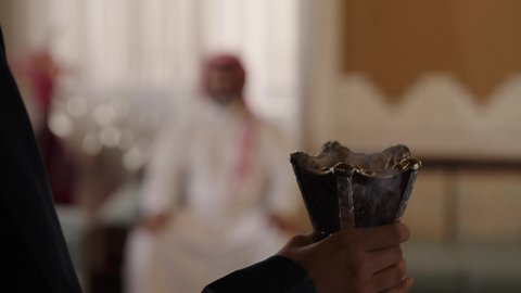 التبخر والتطيب بخشب العود، عادات وتقاليد المجتمع السعودي في الأعياد والمناسبات الاسلامية، عطورات وروائح خليجية مميزة، الاصالة والعراقة والتراث السعودي, تصوير لإمراة عربية خليجية سعودية ترتدي العباءة والحجاب تقوم بتبخير وتعطير والده الكبير بالعمر بالمبخرة