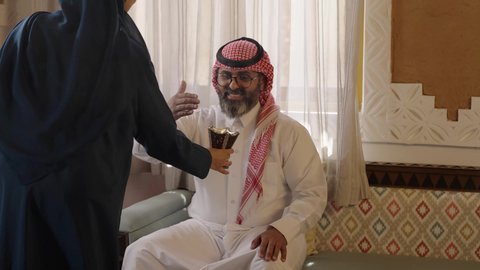 عطورات وروائح خليجية مميزة، الاصالة والعراقة والتراث السعودي, تصوير لإمراة عربية خليجية سعودية ترتدي العباءة والحجاب تقوم بتبخير وتعطير والده الكبير بالعمر بالمبخرة، التبخر والتطيب بخشب العود، عادات وتقاليد المجتمع السعودي في الأعياد والمناسبات الاسلامية