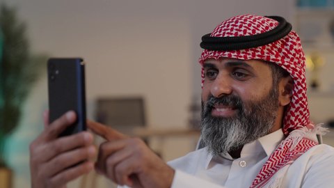 استخدام جهاز تقني حديث, رجل عربي خليجي سعودي يرتدى الثوب والشماغ يستخدم الهاتف المحمول,الدردشة مع الأهل والأصدقاء, دمج التقنية والتكنولوجيا بالحياة اليومية