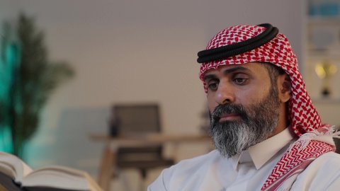 ايماءات التركيز والاستمتاع, الاهتمام بتصفح الكتب المفيدة, تصوير مقرب لرجل عربي خليجي سعودي يرتدى الثوب والشماغ يمسك بيده الكتاب, توسيع المعرفة وتعزيز الثقافة الفكرية