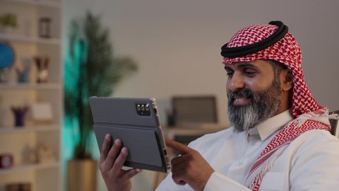 تصفح الانترنت ومتابعه أخبار السوشال ميديا, الدردشة والتواصل مع الاهل والاصدقاء, ,تصوير مقرب لرجل عربي خليجي سعودي يرتدى الثوب والشماغ يقوم بالنقر على جهاز التابلت