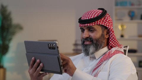 تصفح مواقع التواصل الاجتماعي عبر الانترنت, الدردشة والتواصل مع الاهل والاصدقاء, تصوير مقرب لرجل عربي خليجي سعودي يرتدى الثوب والشماغ يقوم بالنقر على جهاز التابلت