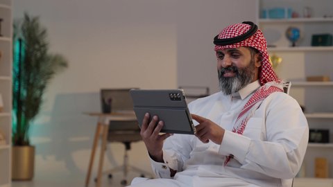 Friendly conversations and chats via modern electronic applications, chatting and communicating with family and friends, a close-up photo of a Saudi Arabian Gulf man wearing a thobe and shemagh, tapping on a tablet, browsing the internet and following social media news.