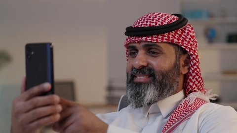 استخدام جهاز تقني حديث، تصوير مقرب لرجل عربي خليجي سعودي يرتدى الثوب والشماغ يقوم بالنقر على الجوال, التواصل والدردشة مع الأهل والأصدقاء, التسوق الإلكتروني وتصفح برامج وتطبيقات التواصل الاجتماع