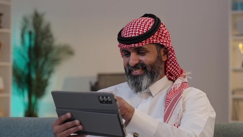 استخدام تطبيقات وبرامج الأجهزة اللوحية ، تصوير مقرب لرجل عربي خليجي سعودي يرتدى الثوب والشماغ يقوم بالنقرعلى جهاز التابلت, التسوق الإلكتروني وتصفح برامج التواصل الاجتماع