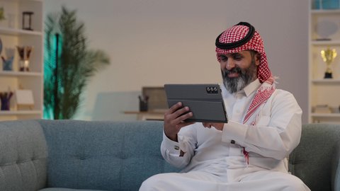 تطور التكنولوجيا والأجهزة التقنية, تصوير مقرب لرجل عربي خليجي سعودي يرتدى الثوب والشماغ يقوم بالنقر على جهاز التابلت, التواصل والدردشة مع الأهل والأصدقاء, التسوق الإلكتروني وتصفح برامج وتطبيقات التواصل الاجتماع