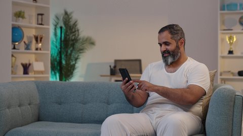 Clicking to select and send files on a mobile phone; integrating technology into practical life; using modern devices to develop personal skills; a Saudi Arabian man wearing trousers and a white undershirt using a mobile phone.