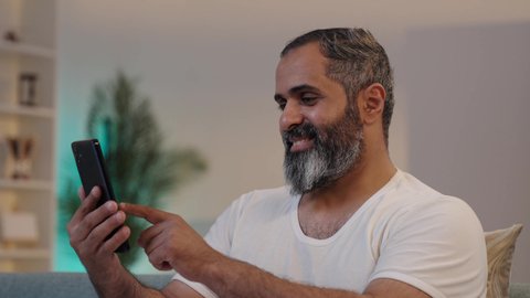 استخدام التطورات والتكنولوجيا الحديثة, دمج التقنية والتكنولوجيا في الحياة اليومية، تصويرمن الجانب لرجل عربي خليجي سعودي يرتدي السروال والفانيله البيضاء يحمل بيده الهاتف المحمول