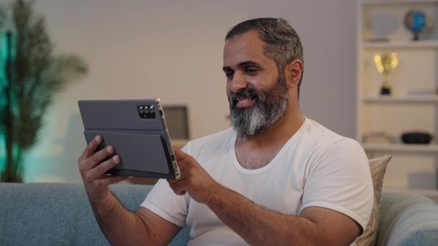 تصفح مواقع التواصل الاجتماعي, الدردشة مع الأهل والأصدقاء، استخدام تطبيقات وبرامج الأجهزة اللوحية، دمج التكنولوجيا والتقنيات الحديثة فى الحياه اليوميه ، تصويرلرجل عربي خليجي سعودي يرتدي السروال والفانيله البيضاء يحمل بيده جهاز التابلت