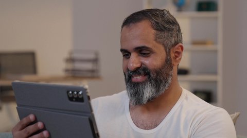 دمج التكنولوجيا والتقنيات الحديثة فى الحياه اليوميه,  استخدام تطبيقات وبرامج الأجهزة اللوحية, تصويرمقرب لرجل عربى خليجى سعودى يرتدى الفانيلة و السروال يحمل بيده جهاز التابلت, قضاء وقت ممتع في المنزل,  تصفح مواقع التواصل الاجتماعي