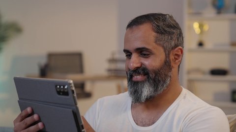 استخدام تطبيقات وبرامج الأجهزة اللوحية, تصويرمقرب لرجل عربى خليجى سعودى يرتدى الفانيلة و السروال يحمل بيده جهاز التابلت, قضاء وقت ممتع في المنزل,  تصفح مواقع التواصل الاجتماعي