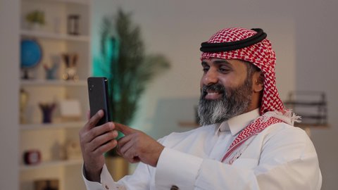 الدردشة مع الأهل والأصدقاء, إستخدام أجهزة تقنية حديثة, تصوير لرجل عربي خليجي سعودي يرتدى الثوب والشماغ يمسك بيده الهاتف المحمول، دمج التقنية والتكنولوجيا بالحياة اليومية
