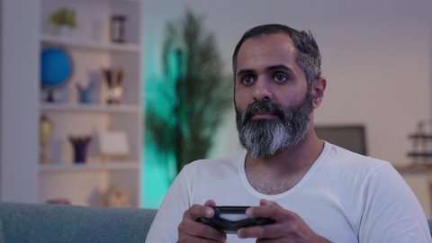 PlayStation games for entertainment, immersion and interaction with the electronic video game, an Arab Gulf Saudi man wearing a t-shirt and trousers holding a controller, spending enjoyable time at home.