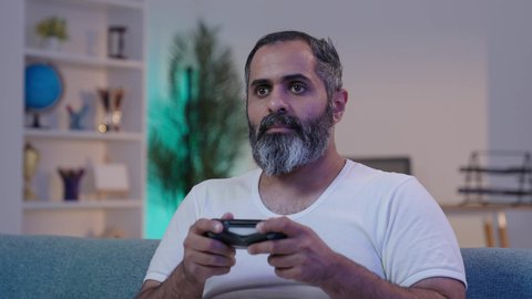 الاندماج والتفاعل مع اللعبة, ايماءات الانسجام و الاستمتاع بالعاب الفيديو الالكترونيه, رجل عربى خليجى سعودى يرتدى الفانيلة و السروال يحمل بيده عصا التحكم