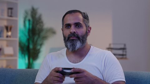 ايماءات الانسجام و الاستمتاع بالعاب الفيديو الالكترونيه, رجل عربى خليجى سعودى يرتدى الفانيلة و السروال يحمل بيده عصا التحكم, الاندماج والتفاعل مع اللعب