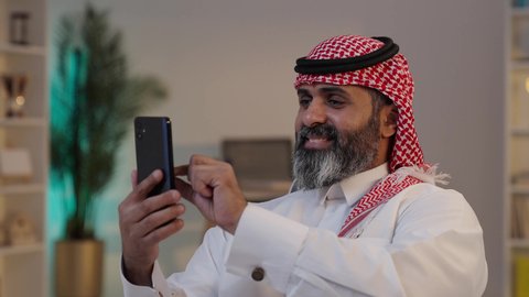 إستخدام أجهزة تقنية حديثة, تصوير لرجل عربي خليجي سعودي يرتدى الثوب والشماغ يمسك بيده الهاتف المحمول, التواصل مع الأصدقاء ، دمج التقنية والتكنولوجيا بالحياة اليومية