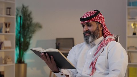 قضاء أوقات الفراغ بالتثقيف والتعلم, حب المطالعة والقراءة، مفهوم التأمل والتفكير, تنمية مهارات القراءة, الاهتمام بتصفح الكتب المفيدة,  تصويرلرجل عربي خليجي سعودي يرتدى الثوب والشماغ يجلس على الاريكة يمسك بيده الكتاب