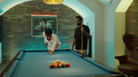الأنشطة الترفيهية للشباب، مفهوم المنافسات والتحديات، قضاء أوقات الفراغ مع الاصدقاء, طاولة بلياردو (السنوكر), شابان عربيان خليجيان سعوديان يرتديان ملابس كاجوال والزي التقليدي يلعبان لعبة البلياردو، صاله رياضيه شبابيه