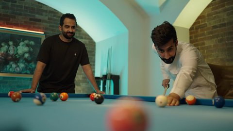 أنشطة شبابية وترفيهية، مفهوم المنافسات والتحديات، قضاء أوقات الفراغ مع الاصدقاء, طاولة بلياردو (السنوكر), شابان عربيان خليجيان سعوديان يرتديان ملابس كاجوال والزي التقليدي يلعبان لعبة البلياردو، صاله رياضيه شبابيه