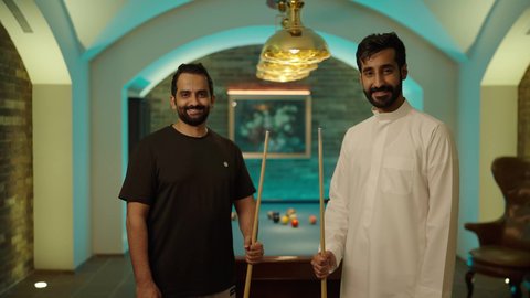 التسلية وقضاء الوقت مع الأصدقاء، مفهوم المنافسات والتحديات, أنشطه وهوايات شبابيه, طاولة بلياردو (السنوكر), شابان عربيان خليجيان سعوديان يرتديان ملابس كاجوال والزي التقليدي يمسكان عصا لعبة البلياردو، صاله رياضيه شبابيه