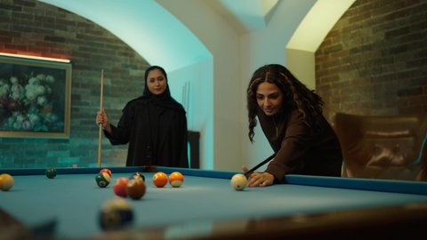 Spending quality time with friends, a youth sports hall, youth activities and hobbies, playing, challenging, and competing, a billiard table (snooker), two Arab Gulf friends playing billiards.