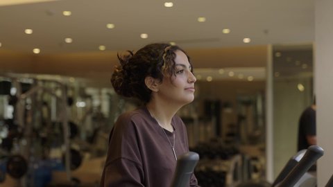 انشطة وتمارين رياضية، امرأة عربية خليجية سعودية ترتدي الملابس الرياضية وتقوم بالتمارين البدنية، استخدام الأجهزة الرياضية، الزي الرياضي النسائي، صالة الألعاب الرياضية، الصحة واللياقة البدنية، مفهوم النشاط بدني