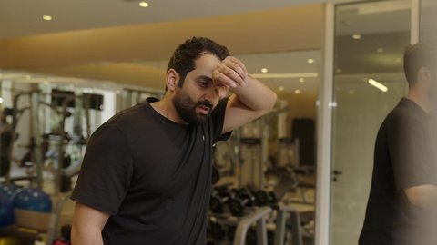 تحمل التمارين القاسية للمحافظة على اللياقة، تقوية العضلات ونحت الجسم, وقت ممتع أثناء التمرين ، أسلوب حياة صحية، استخدام الأجهزة التقنية الحديثة، مفهوم حرق الدهون و إنقاص الوزن، رجل عربي خليجي سعودي يرتدي الملابس الرياضية يقوم بالتمشية على جهاز المشي