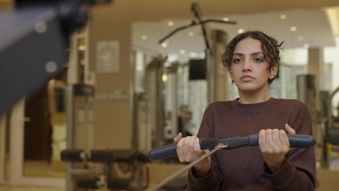 إيماءات السعادة والنشاط، أنشطة بدنية للمحافظة على اللياقة والرشاقة، اتباع أسلوب حياة صحي باستخدام الأجهزة التقنية، رياضات لتقوية العضلات ونحت الجسم، تصوير لشابة عربية خليجية سعودية ترتدي زي رياضي تقوم بممارسة التمارين الرياضية