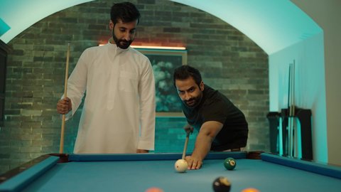 Spending free time with friends, the concept of competitions and challenges, activities and youth hobbies, billiard table (snooker), a group of young Arab Gulf Saudi men wearing casual and traditional clothing playing billiards, a youth sports hall.