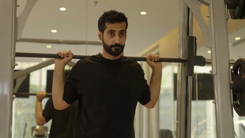 رياضة كمال الأجسام، أسلوب حياة صحي، إيماءات القوة والثقة، الاهتمام بالصحة واللياقة الجسدية، شاب عربي خليجي سعودي يرتدي الزي الرياضي يقوم  بممارفة تمارين رفع الاثقال، استخدام الأجهزة الرياضية، رجل سعودي يمارس أنشطة لتقوية العضلات
